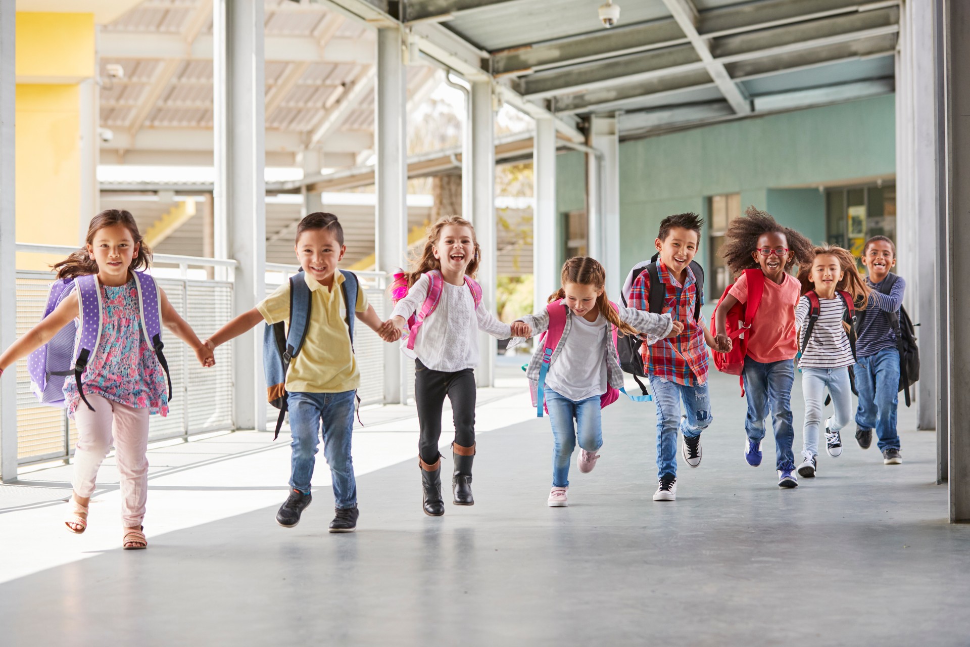 Primary school kids run holding hands in corridor, close up